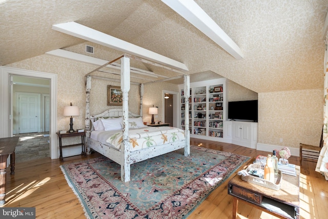 bedroom with hardwood / wood-style floors, vaulted ceiling, and a textured ceiling