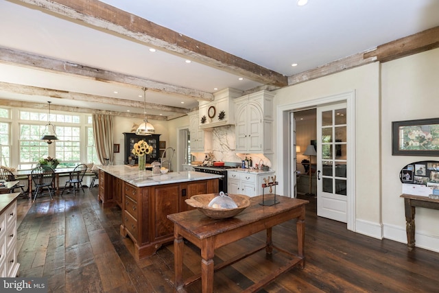 kitchen with pendant lighting, high end stainless steel range oven, a kitchen island with sink, light stone countertops, and beamed ceiling