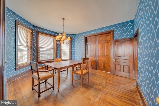 dining space featuring wallpapered walls, a notable chandelier, baseboards, and wood finished floors