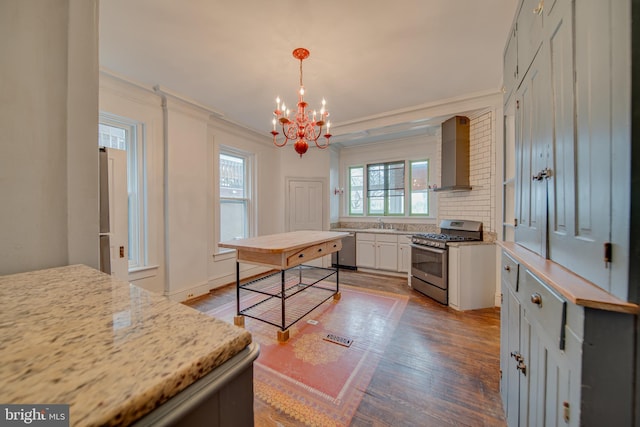 kitchen featuring crown molding, appliances with stainless steel finishes, white cabinetry, hanging light fixtures, and wall chimney exhaust hood