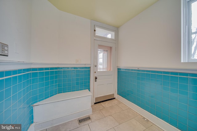 interior space featuring tile patterned floors, plenty of natural light, tile walls, and wainscoting