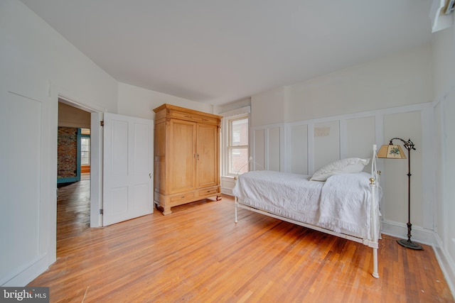 bedroom featuring light wood-type flooring, wainscoting, and a decorative wall