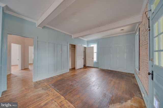 empty room featuring ornamental molding, wood-type flooring, beam ceiling, and brick wall