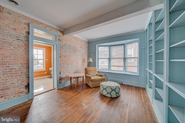 living area with ornamental molding, beam ceiling, brick wall, and wood finished floors