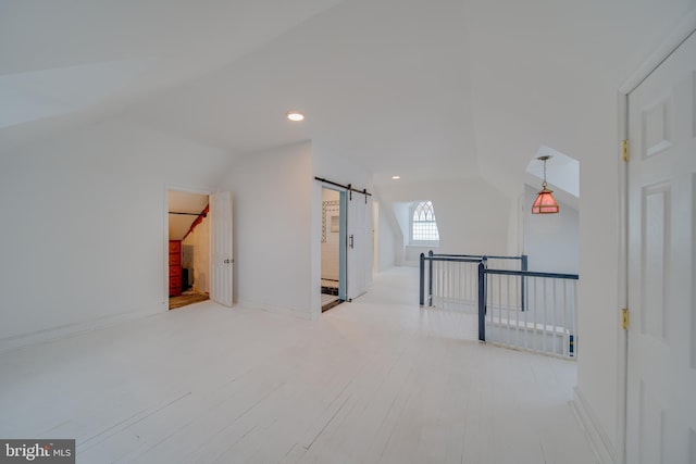 additional living space with a barn door, baseboards, wood finished floors, vaulted ceiling, and recessed lighting