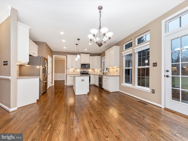 kitchen featuring white cabinetry, a center island, hanging light fixtures, stainless steel appliances, and decorative backsplash