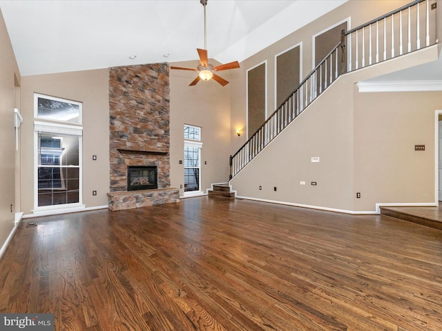 unfurnished living room with ceiling fan, wood-type flooring, a fireplace, and a towering ceiling