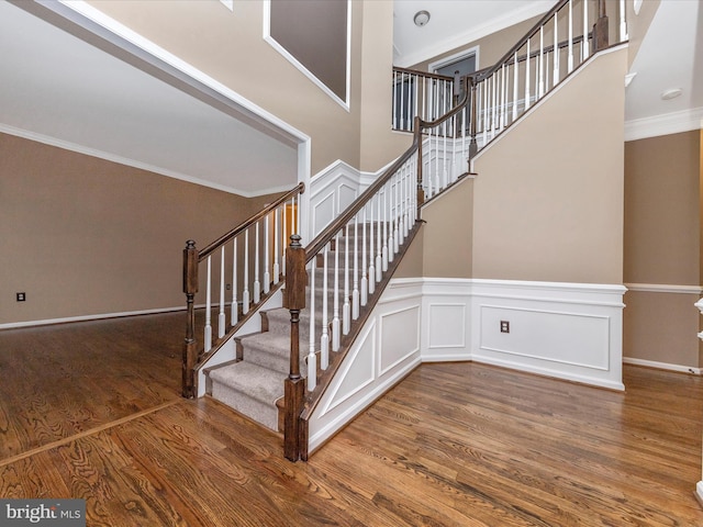 staircase with ornamental molding, wood-type flooring, and a towering ceiling