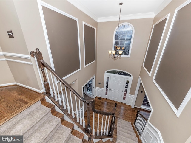 foyer featuring an inviting chandelier, ornamental molding, wood-type flooring, and a high ceiling