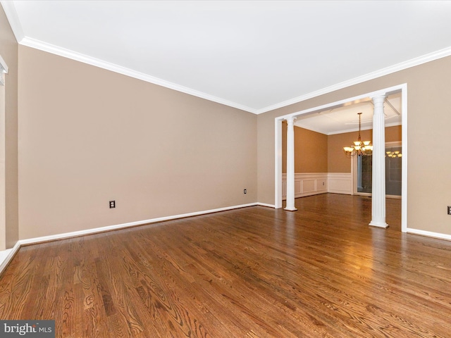 empty room featuring crown molding, wood-type flooring, a chandelier, and ornate columns