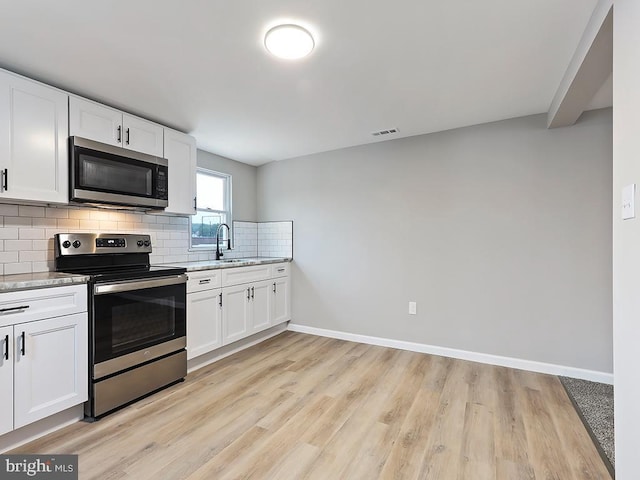 kitchen with sink, white cabinetry, stainless steel appliances, light stone countertops, and decorative backsplash