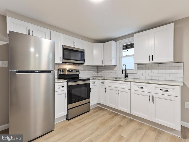 kitchen with tasteful backsplash, sink, white cabinets, stainless steel appliances, and light wood-type flooring