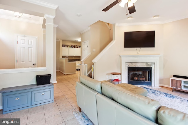 living room with ornate columns, crown molding, light tile patterned floors, ceiling fan, and a premium fireplace