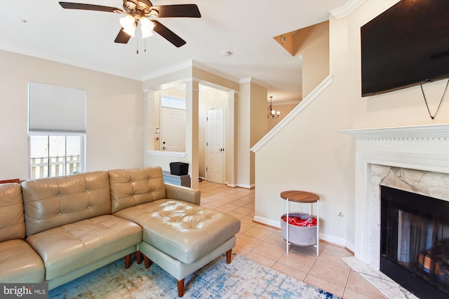 tiled living room featuring ceiling fan with notable chandelier, a high end fireplace, ornamental molding, and ornate columns