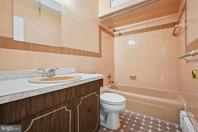 full bathroom with baseboard heating, tile walls, vanity, tiled shower / bath, and toilet