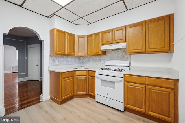 kitchen with tasteful backsplash, white gas range, light hardwood / wood-style floors, and a drop ceiling