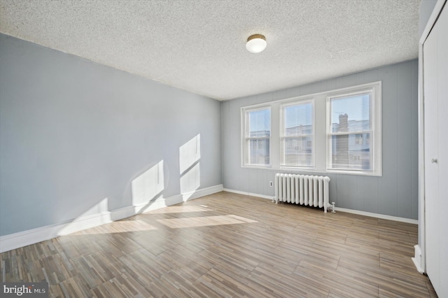 spare room featuring radiator heating unit, a textured ceiling, and light wood-type flooring