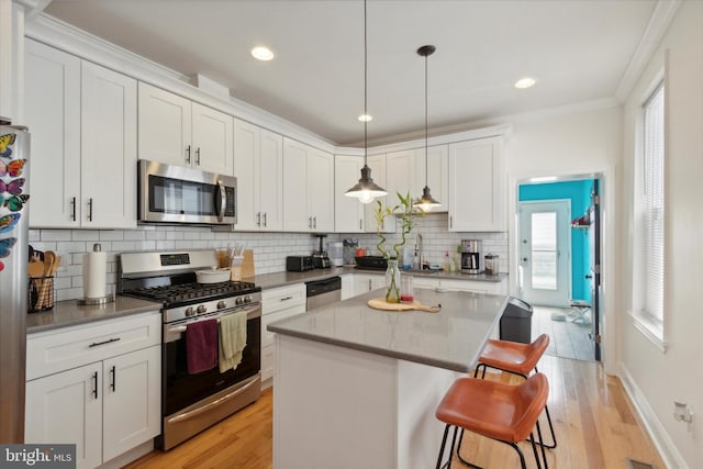 kitchen with a kitchen island, white cabinetry, a kitchen bar, hanging light fixtures, and stainless steel appliances