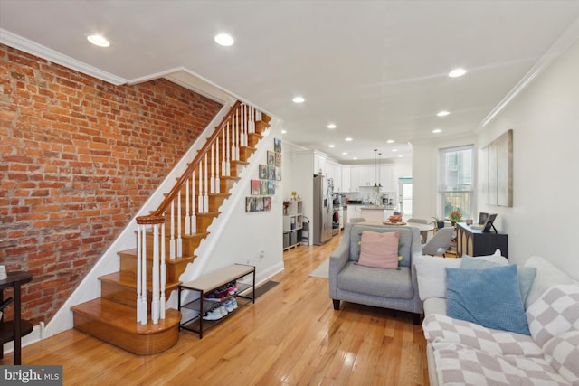 living room with light hardwood / wood-style flooring, ornamental molding, and brick wall