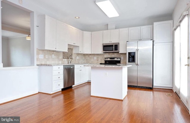 kitchen with appliances with stainless steel finishes, light stone counters, light hardwood / wood-style floors, white cabinets, and decorative backsplash