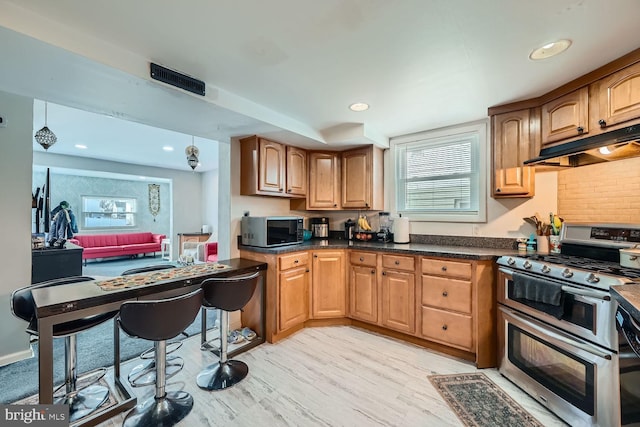 kitchen featuring double oven range, decorative light fixtures, light hardwood / wood-style flooring, and backsplash