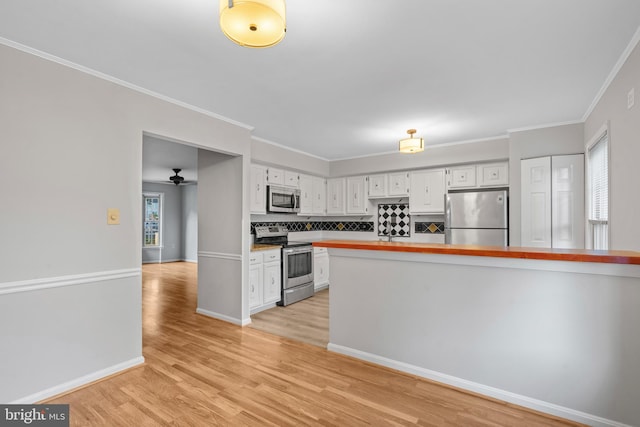 kitchen featuring crown molding, light hardwood / wood-style flooring, appliances with stainless steel finishes, white cabinets, and decorative backsplash