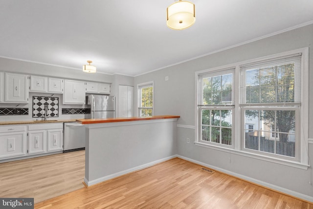 kitchen with crown molding, kitchen peninsula, stainless steel appliances, light hardwood / wood-style floors, and white cabinets