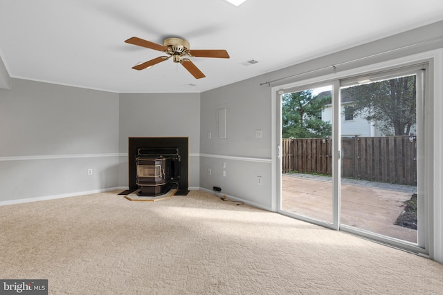 unfurnished living room with ceiling fan, carpet flooring, and a wood stove