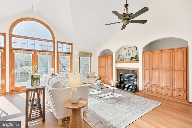 living area featuring light wood-style flooring, high vaulted ceiling, ceiling fan, and a tiled fireplace