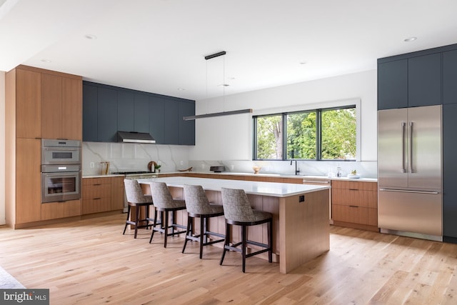 kitchen featuring a center island, hanging light fixtures, light wood-type flooring, appliances with stainless steel finishes, and a kitchen breakfast bar