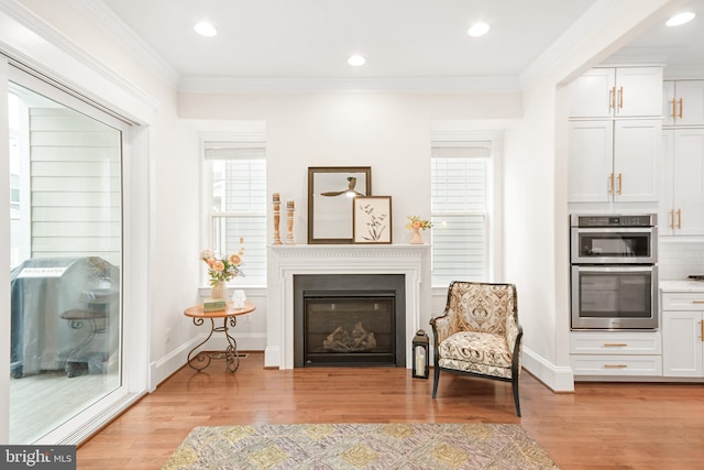 living area featuring a glass covered fireplace, baseboards, crown molding, and light wood finished floors