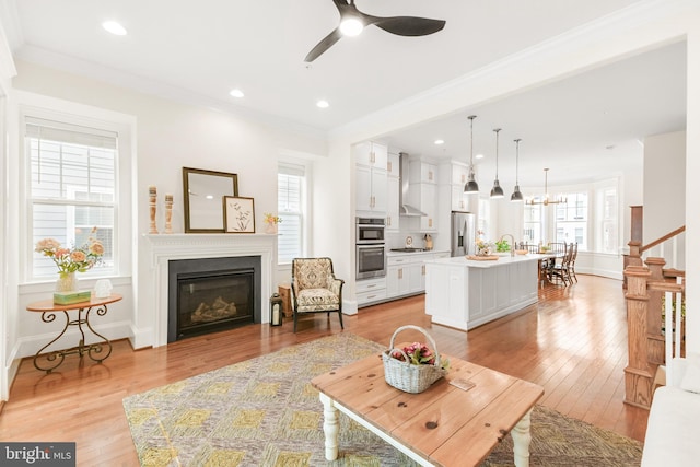 living room with baseboards, a glass covered fireplace, ornamental molding, light wood-style floors, and recessed lighting