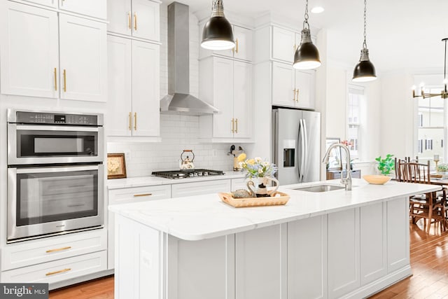 kitchen with a center island with sink, white cabinets, appliances with stainless steel finishes, wall chimney range hood, and a sink