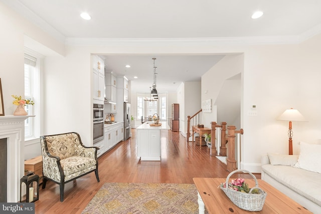 living room featuring stairs, crown molding, an inviting chandelier, and wood finished floors