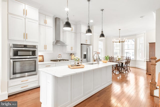 kitchen featuring tasteful backsplash, light wood finished floors, wall chimney exhaust hood, and stainless steel appliances