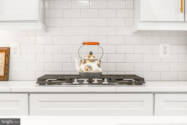 kitchen with stainless steel gas stovetop, white cabinetry, and backsplash