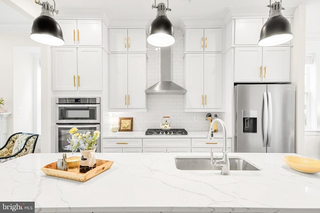 kitchen featuring backsplash, appliances with stainless steel finishes, white cabinetry, a sink, and wall chimney range hood