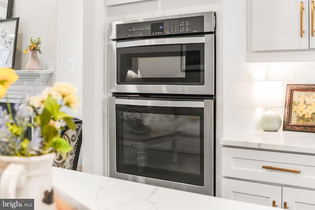 kitchen with double oven, tasteful backsplash, white cabinetry, and light stone countertops