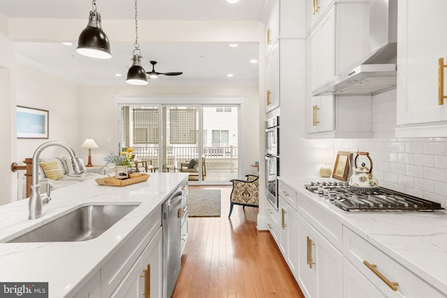 kitchen with white cabinets, wall chimney exhaust hood, a sink, stainless steel appliances, and backsplash