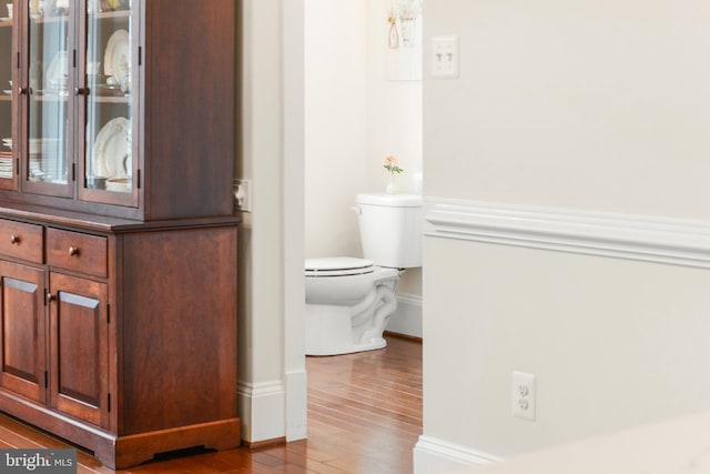 half bathroom with toilet, baseboards, and wood finished floors