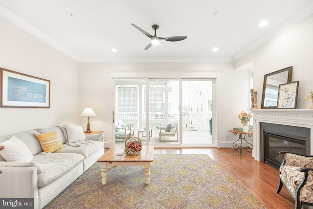 living area with baseboards, ornamental molding, wood finished floors, and a glass covered fireplace