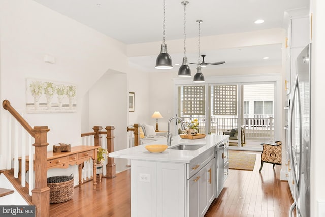 kitchen with stainless steel appliances, light wood-style flooring, a kitchen island with sink, white cabinets, and a sink