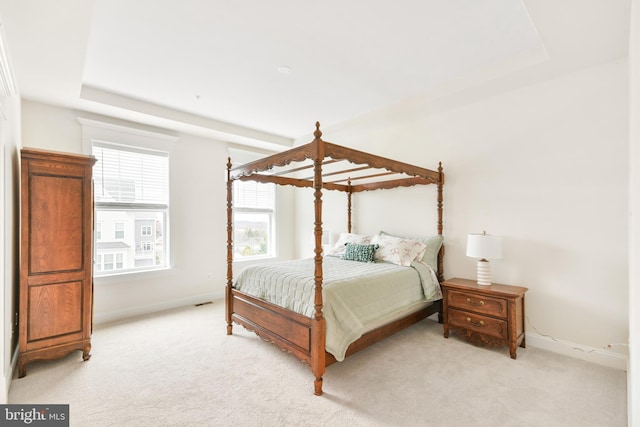 bedroom featuring light carpet, a tray ceiling, and baseboards