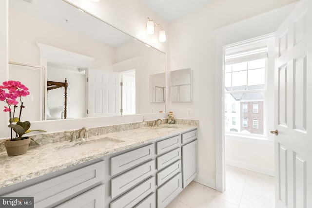 full bathroom featuring marble finish floor, double vanity, a sink, and baseboards