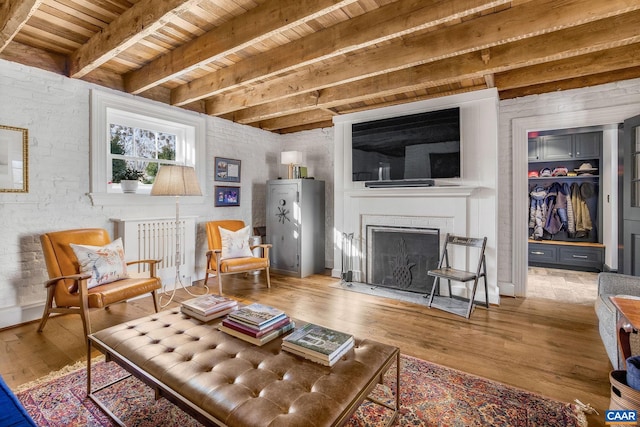 living room with radiator heating unit, wood-type flooring, brick wall, wooden ceiling, and beamed ceiling