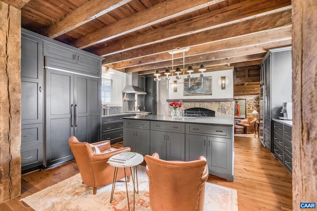 kitchen with gray cabinets, hanging light fixtures, beam ceiling, wall chimney range hood, and light wood-type flooring