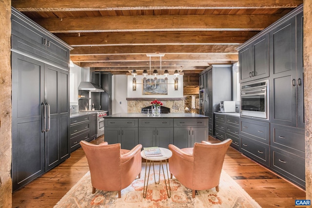 kitchen with pendant lighting, wall chimney range hood, appliances with stainless steel finishes, light hardwood / wood-style floors, and beamed ceiling