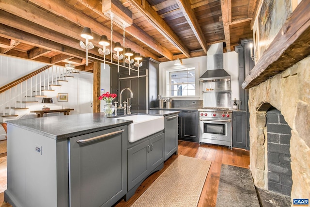 kitchen featuring wall chimney range hood, sink, gray cabinets, a kitchen island with sink, and stainless steel appliances