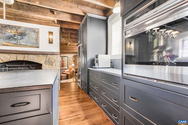 kitchen featuring a stone fireplace, light hardwood / wood-style flooring, wooden ceiling, beam ceiling, and oven