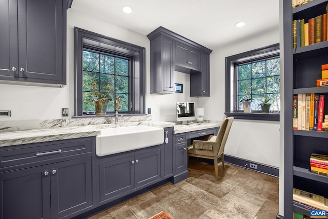 kitchen featuring sink, built in desk, and light stone counters